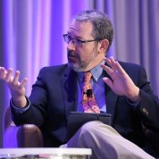 Dr. Gordon, seated on stage, talks to panelist with open palms