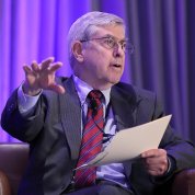 Dr. Koroshetz, seated, speaks with outstretched hand while holding papers in the other.