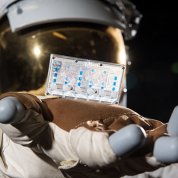 An astronaut in a space suit holds out a small plastic card containing human cells for study.