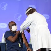 An African American man sits with rolled-up sleeve as a nurse in a white lab coat injects a needle into his arm at the Clinical Center.