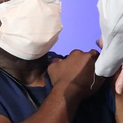 An African American man sits with rolled-up sleeve as a nurse in a white lab coat injects a needle into his arm at the Clinical Center.