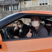 Jen and Luke give thumbs up sitting in Driven to Cure car in front of the Children's Inn.