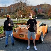 Luke (r) and his father pose with the orange sportscar with a license plate that reads F Cancr, with the Clinical Center behind them.