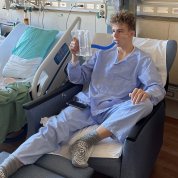Luke, sitting in chair in his Clinical Center room, uses a spirometer to work out his lungs after his kidney surgery.