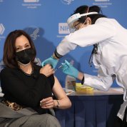 Seated with left arm exposed, Harris receives a shot in the arm from Judy Chan.