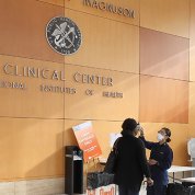 Panoramic view of hospital lobby with uniformed nurse taking temperature of employee entering building.