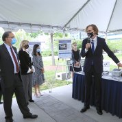 Tromberg stands in front of a display table and speaks to several senators under a tent