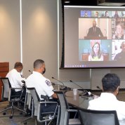 Male speaker at podium in conference room with uniformed officers seated around table looking at projector screen