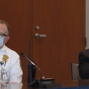 Seated at conference table in facemasks, male in police uniform and male in suit