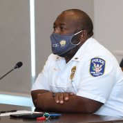 Black male in uniform and facemask, seated at conference table