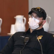 White male in police uniform and cap with sunshades on brim, wearing face mask