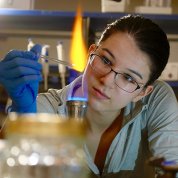 Closeup image of woman with lab-gloved hand holding an eyedropper over an open flame.
