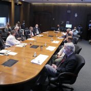 Conference room with people in masks seated around table and in chairs along the perimeter
