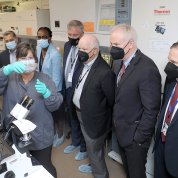 Woman in mask holds up glass flasks in gloved hands as masked people look on