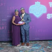 Johnson and mom hold ceremonial football, with NFL draft venue backdrop behind them