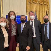 group photo of five individuals in face masks with the East Room of the White House behind them.