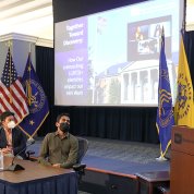 White speaks from podium, as panelists observe