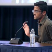 Seated at panel table, Patel speaks into mic.