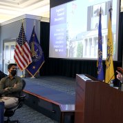 Levine speaks at an NIH podium, with event title slide projected on screen beside her