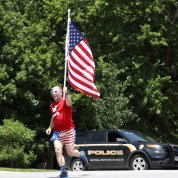 An NIH'er in red shirt and U.S. flag-patterned shorts crosses the street holding an American flag