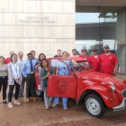 A group of health professionals stand around the red Volkswagen Beetle. Two of them are behind an open door