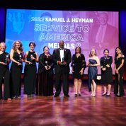 Winners stand on the stage with their trophies in front of a screen that reads 2022 Samuel J. Heyman Service to America Medals 