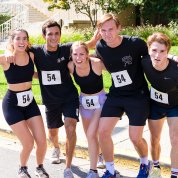 Five runners, linking shoulders, smile into camera.