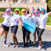 Five women wearing wigs and sunshades in dayglo colors of the rainbow, strike humorous poses.