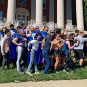 Large group of runners and supporters pose in profile with fist pumps in front of Bldg. 1