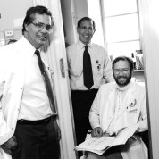 Three men, two in lab coats, smile at camera from doorway to laboratory