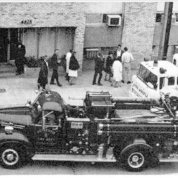 A black & white photo shows a fire truck and ambulance outside a building off campus
