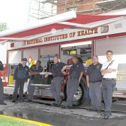 A group of firefighters pose leaning against an NIH fire truck
