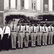 Black & white photo of fire department staff standing next to fire truck in front of Bldg. 1