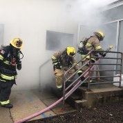 Three fire fighters in uniform walking into smoky building with hose on NIH campus, as part of a training exercise