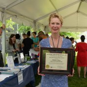 Liles, standing inside tent, holds her framed NIH safety award.