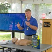 a DOHS rep stands by table with a defibrillator and mannequin, talking about CPR.