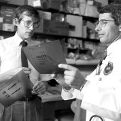 Black & white image. With lab behind them, Lane and Fauci look over a document held by Fauci