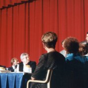 Fauci stands at podium on stage with conference table where Reagan is seated with several other dignitaries.