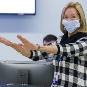 Damiano in checkered dress extends her arms straight in front of her.