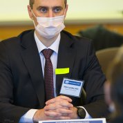 Ukraine's health minister wearing a mask, sits with hands folded at table in CC medical board room, listening intently to NIH staff briefing.
