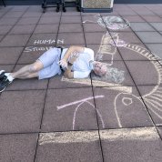 A man lies on ground beside microscope drawn in colorful chalk and the words "human studies"