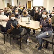 Group of fellows seated at table, two of them holding up the 2-finger peace sign