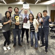 A group of fellows stand smiling, holding their awards, in a conference room.