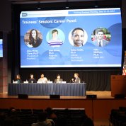 Panelist sit on stage underneath a large projector screen