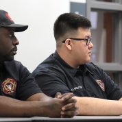 Two officers, one African American, one Asian, sit with hands clasped, listening.