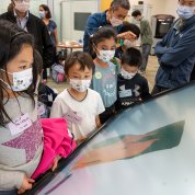 Four masked children look down at a large screen in the NIH Library.
