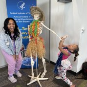 Mother and daughter pose with skeleton model wearing leis and grass skirt.