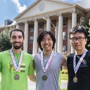 The first three race finishers smile with their medals in front of Building 1. 