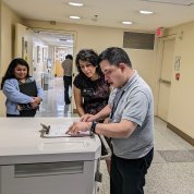 Van Berg, in a gray polo shirt, points to a clipboard on a desk as Wolek and another woman look on.