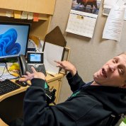 Day, wearing a black hoodie, looks up from his desk. His hands are poised over his computer keyboard.